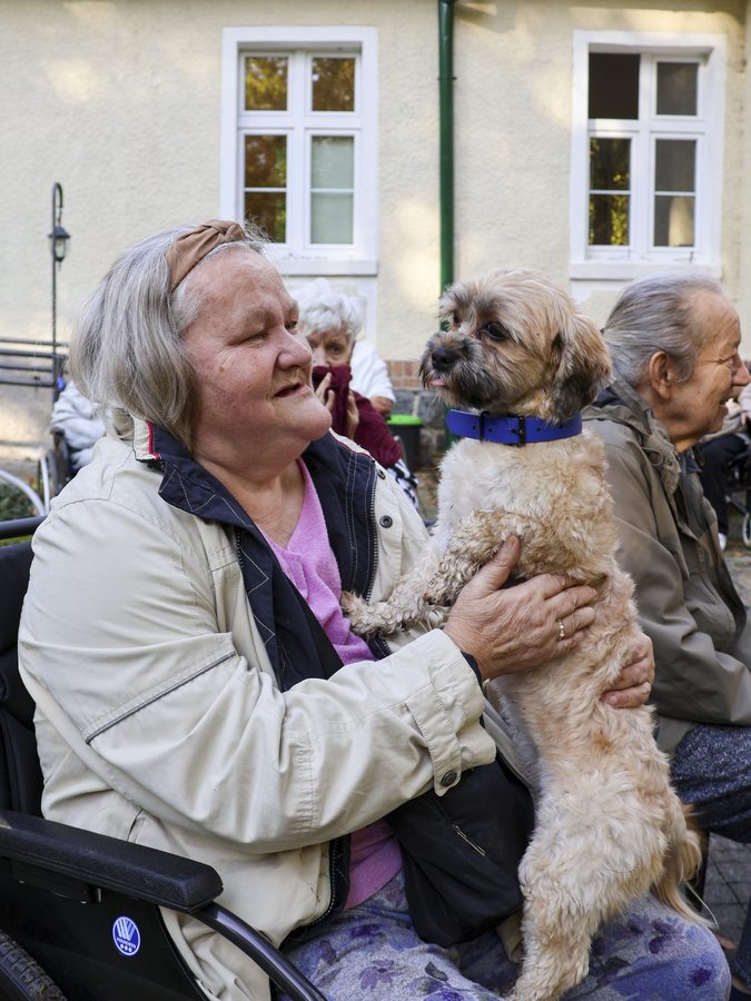 Seniorka trzyma małego psa na kolanach przed budynkiem Rezydencji