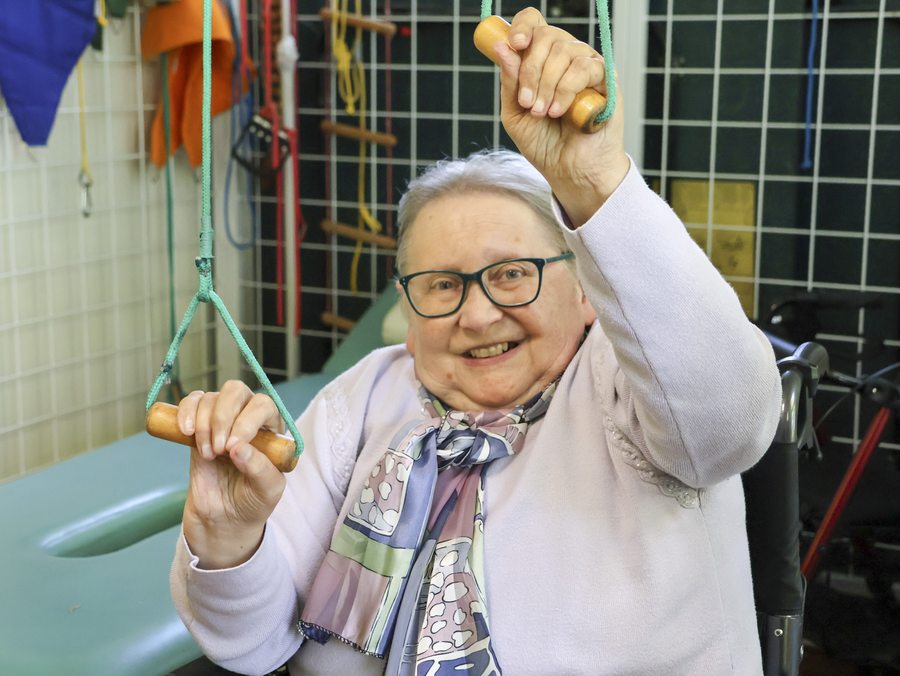 Seniorka korzysta z przyrządów do ćwiczeń w sali rehabilitacyjnej